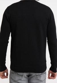 Maglione nero con maniche lunghe, polsini e orlo a costine. Tessuto a maglia liscia, design minimalista, cuciture visibili sulla spalla.