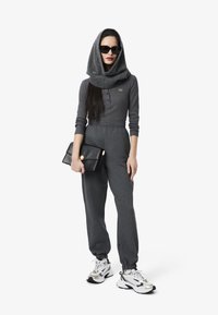 Ensemble de sport gris composé d'un haut à manches longues et d'un pantalon à taille élastique, associé à des baskets blanches. Sac à main noir et lunettes de soleil surdimensionnées.