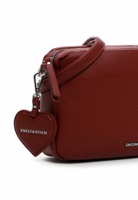 Bolso cruzado de cuero rojo con textura de guijarros, cierre de cremallera, correa ajustable y un prominente charm en forma de corazón con el logo "EMILY&NOAH".