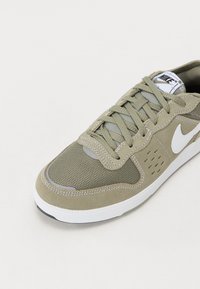 Sapatilha verde com materiais em malha e camurça, logotipo branco, design de atacadores, gola almofadada e detalhes texturizados na parte superior.