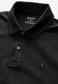 Polo shirt negro de corte ajustado confeccionado en algodón. Presenta un cuello con solapa, dos botones y un pequeño diseño bordado de un ciervo en el pecho.