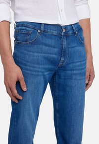 Jeans in denim blu con taglio dritto, design a cinque tasche e cuciture chiare. Tessuto di alta qualità con una texture liscia.