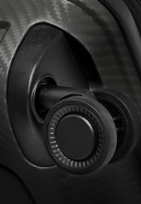 Gros plan sur un bouton rotatif noir avec prise texturée, monté sur une surface texturée en fibre de carbone, probablement une partie d'un panneau de commande de véhicule ou de machine.