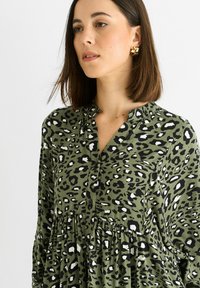Green leopard print blouse with a collared neckline, button closure, and gathered waistline; made from lightweight, textured fabric.
