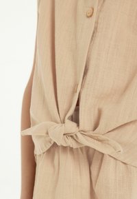 Beige linnen top met een geknoopte voorkant, voorzien van knopen en een zachte, textuurstof. Casual ontwerp met een ontspannen pasvorm.
