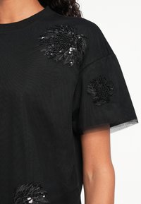 T-shirt nero con tessuto testurizzato, maniche corte e decorazioni floreali in paillettes sulla parte anteriore per un tocco di originalità.