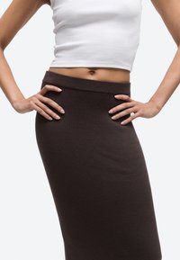 Woman wearing a fitted dark brown ribbed skirt and a white cropped tank top with hands resting on hips.