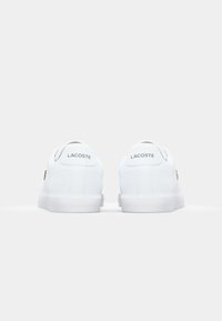 Bijele Lacoste tenisice s glatkom kožnom površinom, ravnim bijelim potplatom i suptilnim brandingom na peti. Minimalistički dizajn s zaobljenim oblikom.