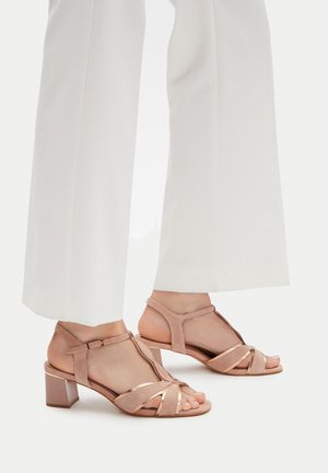 Sandalias de tacón de ante rosa con diseño de tira en T, punta abierta y tacón ancho. Presentan tiras cruzadas y detalles metálicos. Adecuadas para ropa formal.