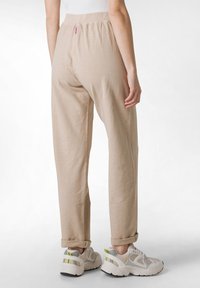 Beige, avslappnade byxor med mjuk textur, elastisk midja och uppvikta knyt, kombinerat med vadderade, ljusa sneakers.