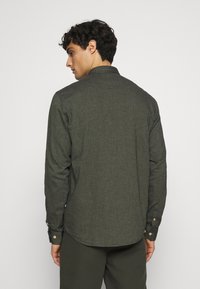 Langarmhemd aus dunkelgrünem Stoff, mit einem Knopfkragen und strukturierter Oberfläche. Knöpfe an den Manschetten und einem abgerundeten Saumdesign.