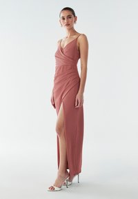 Gara, rozā krāsas kleita ar iešūtu dizainu, darināta ar drapētām tekstūrām un sānu šķēlumu, kombinēta ar baltām augstpapēžu sandaletēm.