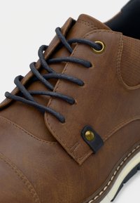 Pruun sünteetilisest nahast king, millel on meresinisest paelad, metallist silmused ja tekstuuriga viimistlus. Kaasa arvatud kontrastne valge tallaosa.