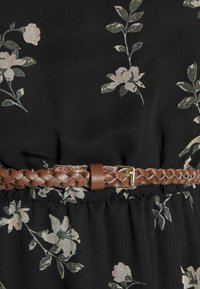 Musta mekko kukkakuviolla, jossa on kerätty vyötärö; varustettu ruskealla punotulla nahkavyöllä, jossa on kultainen solki. Pehmeä kangas, jossa on sileä pinta.