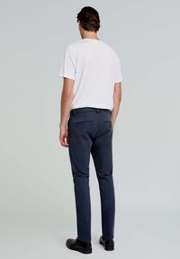 Heren kledingset; een wit t-shirt, marineblauwe chinos met twee achterzakken en een riem, gecombineerd met zwarte schoenen. De outfit heeft een minimalistisch ontwerp.