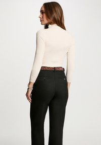 Maglione a collo alto a coste di colore crema abbinato a pantaloni neri a vita alta con una cintura con stampa leopardata, che mostra una silhouette aderente.