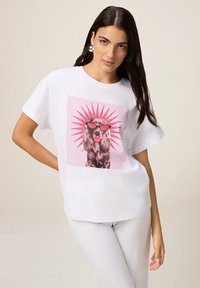 Witte katoenen T-shirt met een grafiek van een leeuw die rode zonnebril draagt, omringd door een roze zonnestraal ontwerp. Relaxte pasvorm met korte mouwen.