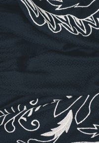 Tissu bleu foncé avec des motifs floraux et de vigne brodés en blanc, légèrement froissé, mettant en valeur la texture et les détails de couture délicats.