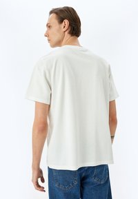 Camiseta de algodón blanca con mangas cortas, cuello redondo y un corte relajado, combinada con vaqueros de denim azul. Textura suave, diseño minimalista.