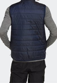 Navy blue puffer vest with quilted design, lightweight fabric, standing collar, and side zip pockets. Worn over a gray long-sleeve shirt.