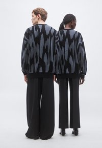 Preveliki črno-sivi pleteni puloverji imajo drzen abstraktni vzorec. Kombinirani z širokimi črnimi hlačami tkanina deluje mehka in teksturirana.