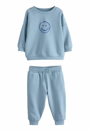 Lichtblauwe sweatshirt en bijpassende joggers van zachte stof. De sweatshirt heeft een smiley-gezichtsafbeelding in het midden; de broek heeft een elastische tailleband.