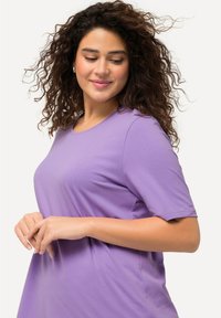 Top corto lavanda a maniche corte realizzato in tessuto morbido, con scollo rotondo e vestibilità rilassata, caratterizzato da morbide pieghe e una texture liscia.