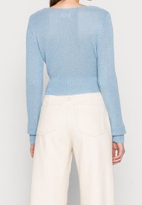 Maglione lavorato a maglia di colore blu chiaro con maniche lunghe, texture a costine e orlo corto, abbinato a pantaloni larghi di colore crema con tasche posteriori.