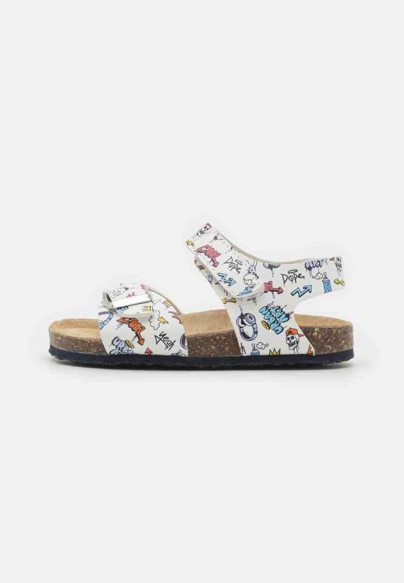 Flerfarget sandal med et hvitt mønstrete overlær som har grafikk, kork fotbed, og en slitesterk svart såle. Åpen tå-design med ankelrem.