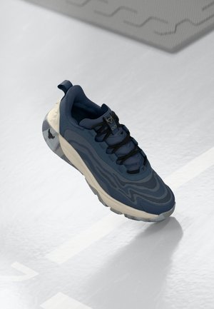 Navy blue sneaker with textured fabric, wave-like design, black laces, and a cream rubber sole. Features logo accents and a cushioned collar.