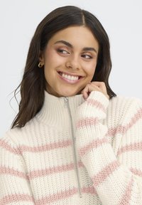 Suéter de punto con un alto cuello, que presenta franjas horizontales en rosa claro y crema. Incluye una cremallera en la parte delantera y puños acanalados.