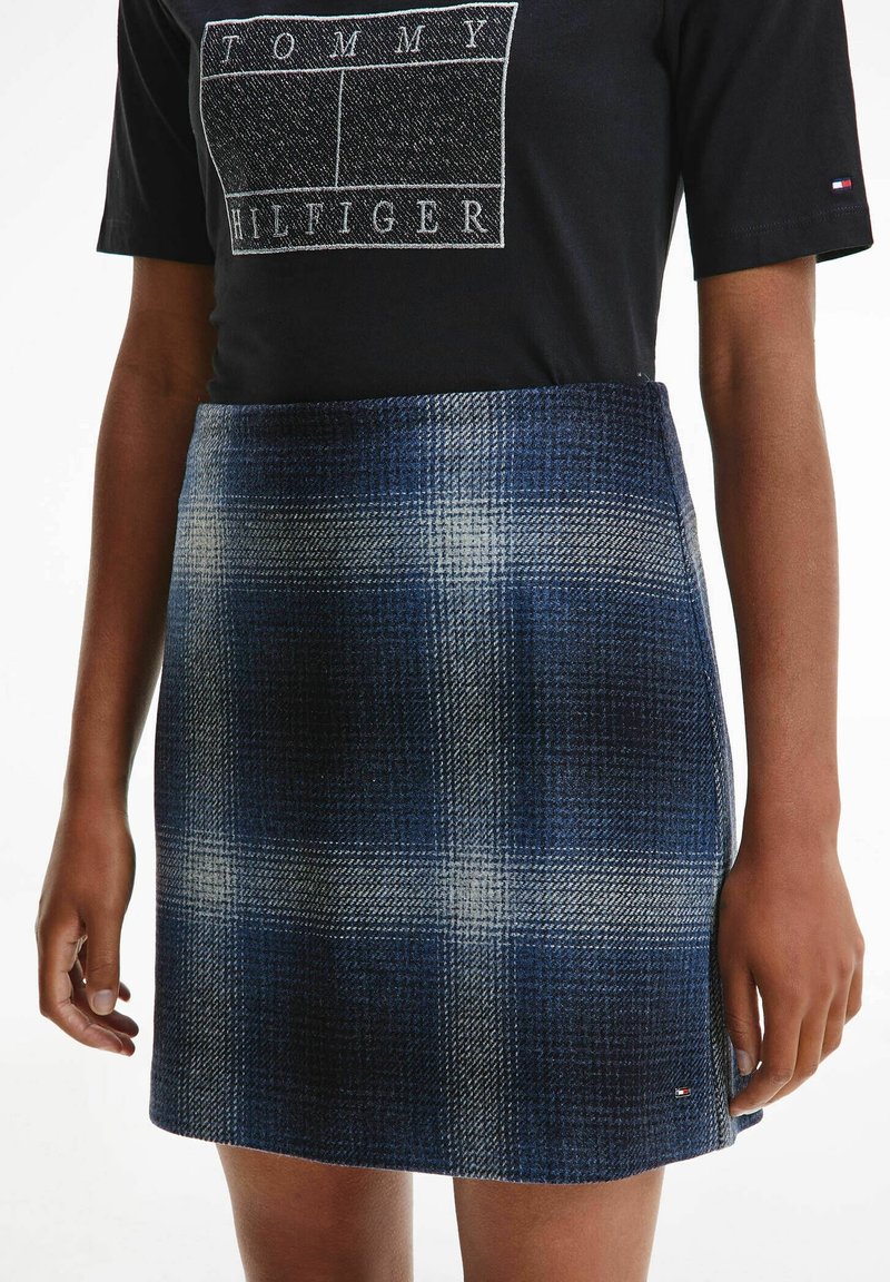 Jupe à carreaux bleus en tissu texturé avec une coupe ajustée. Présente des lignes blanches en grille et une petite étiquette logo sur l'ourlet.