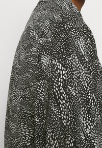 Svart skjorta med ett abstrakt vitt mönster, med varierande former och texturer, designad med krage och korta ärmar.