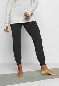 Pantaloni jogger neri con polsini elastici e una texture morbida e liscia, abbinati a una maglietta grigia chiara a maniche lunghe con fori per il pollice.