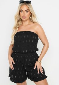 Svart, axelbandslös jumpsuit med texturerad tyg, metallisk guldrandmönster, volangkant och elastisk midja.