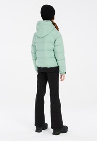 Mintgrüner Pufferjacke mit Kapuze, gerippten Bündchen und schwarzen Akzenten. Kombiniert mit schwarzen gemusterten Hosen und schwarzen Plateauschuhen.