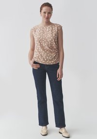 Mouwloze top met stippen in zachte perzikstof met witte stippen. Gecombineerd met donkerblauwe jeans en lichtgekleurde instap schoenen. Eenvoudig ontwerp.