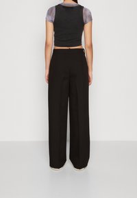 Černé široké kalhoty s vysokým pasem, které mají ostré záhyby a hladkou texturu látky. Nosené s krátkým šedým topem.