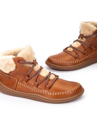 Botas de cuero marrón hasta el tobillo con forro de borreguillo, cordones trenzados en marrón y blanco, y costuras contrastantes distintivas a lo largo de la suela.
