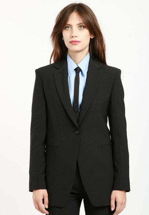 Schwarzer, taillierter Blazer mit strukturierten Schultern, einreihiger Knopfschluss und geschlitzten Revers. Kombiniert mit einem hellblauen Hemd und einer schwarzen Krawatte.
