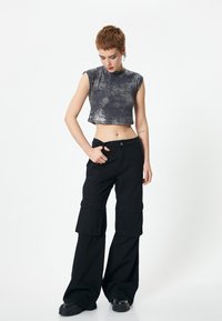 Top corto plateado con un acabado texturizado, combinado con pantalones cargo negros de tiro alto que presentan bolsillos laterales y piernas holgadas.