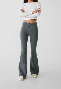Grijze uitlopende jeans met een hoge taille, gemaakt van denimstof. Draagt een cropped witte top met lange mouwen en lichte schoenen.