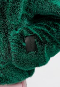 Grüner Kunstfellstoff mit einer weichen Textur, versehen mit einem schwarzen Lederetikett, das auf dem Ärmel mit "AIR JORDAN" geprägt ist.