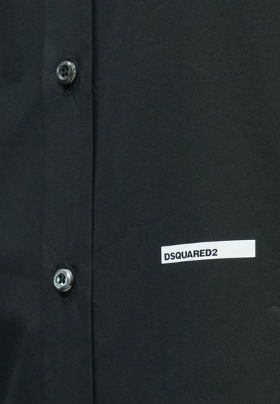 Chemise noire à boutons avec un bouton brillant et une étiquette blanche portant l'inscription "DSQUARED2", mettant en valeur un design élégant et minimaliste.