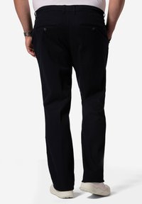 Marinblå byxor med rak bendesign, bakfickor med knappstängning och en slät tygtextur. Bärs med ljusfärgade sneakers.