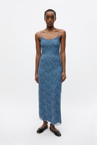 Blue floral patterned maxi dress with thin straps, a fitted silhouette, and slight sheerness. Model paired it with black footwear.