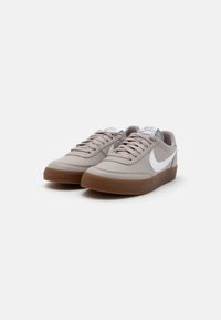Pilki odiniai sportbačiai su lygiu paviršiumi ir rudos gumos padu, su balta Nike swoosh emblema ir lygiais raišteliais.