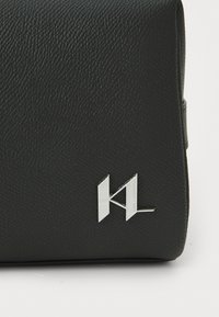 Fekete, texturált bőr táska ezüst színű fém logó akcentussal. Téglalap alakú és elegáns kialakítású, fedeles záródással.