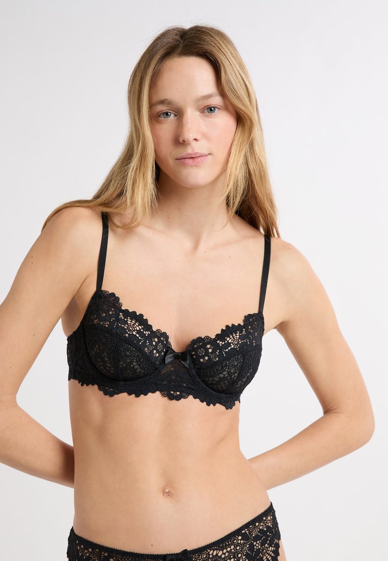 Schwarzer Spitzen-BH mit Bügeln, Blumenmuster, gewellten Rändern und einer zarten Schleife in der Mitte. Dünne verstellbare Träger.