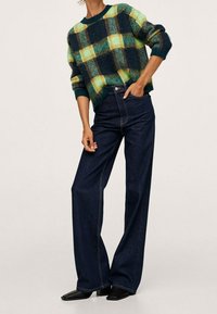 Groen en marineblauw geruite trui met een ronde hals, gecombineerd met hooggetailleerde donkerblauwe wijde jeans en zwarte puntige schoenen.